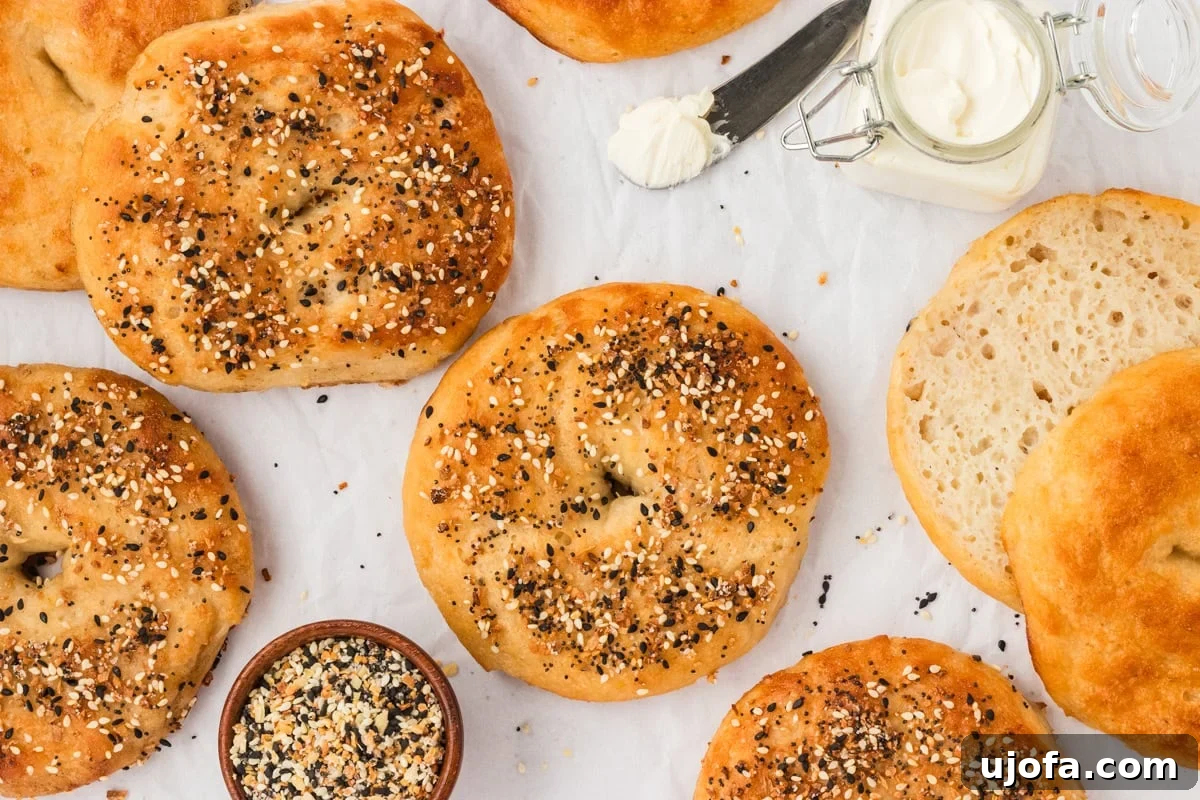 Overhead shot of freshly baked gluten-free bagels on parchment paper, with a dish of everything bagel seasoning, a jar of cream cheese, and one bagel sliced open to show the soft crumb inside.