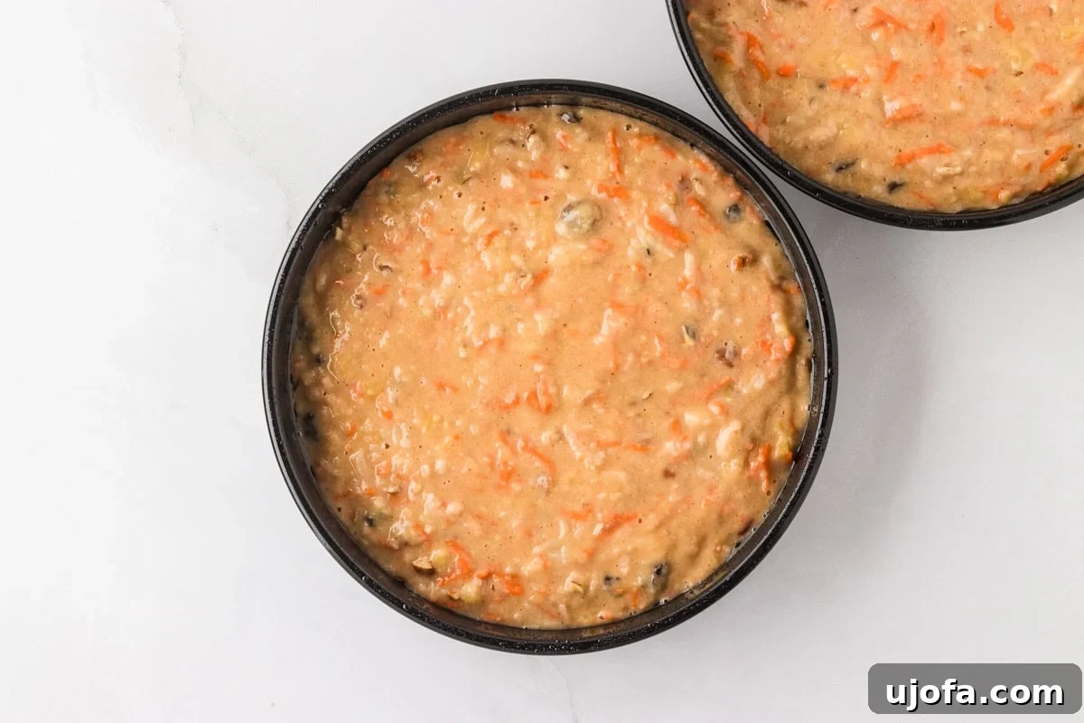 Two round cake pans filled with raw gluten-free carrot cake batter, showing the vibrant orange from shredded carrots and flecks of pecans.