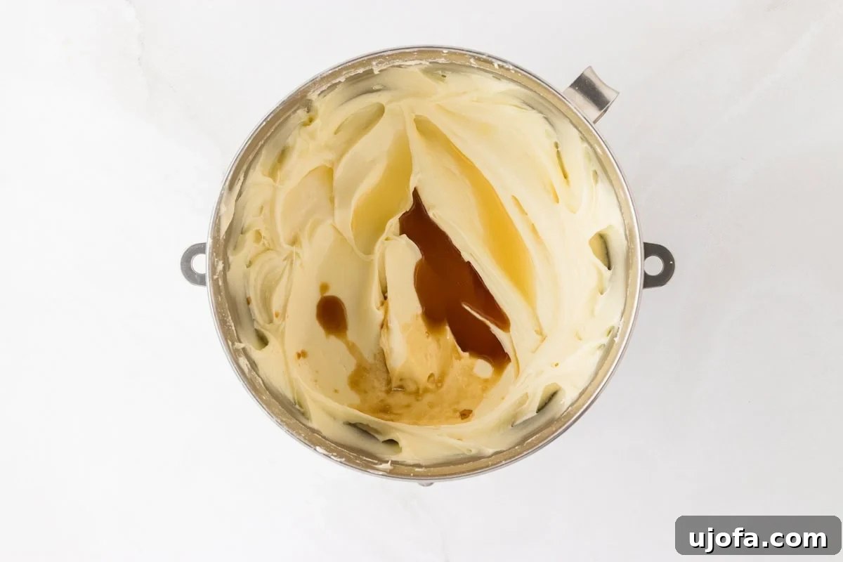 A mixing bowl of cream cheese frosting with vanilla extract added, ready to be blended for extra flavor.