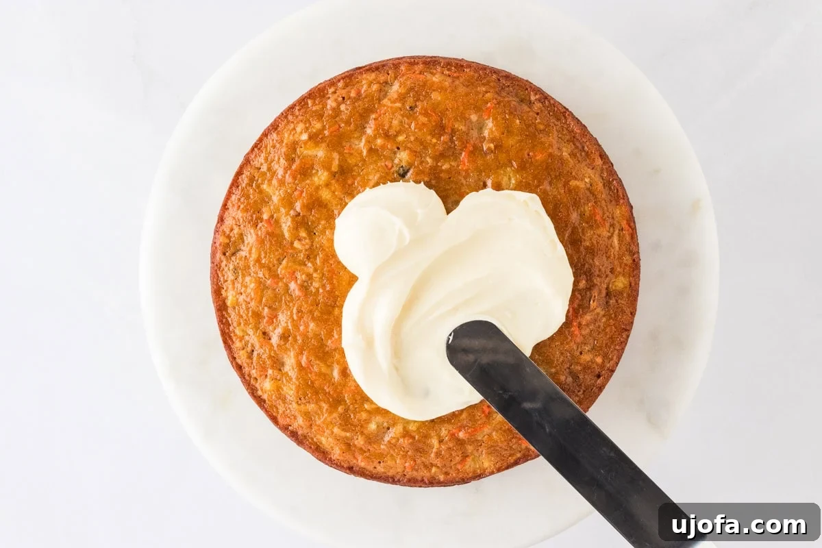 A single layer of gluten-free carrot cake on a cake stand, with a dollop of cream cheese frosting being spread on top.