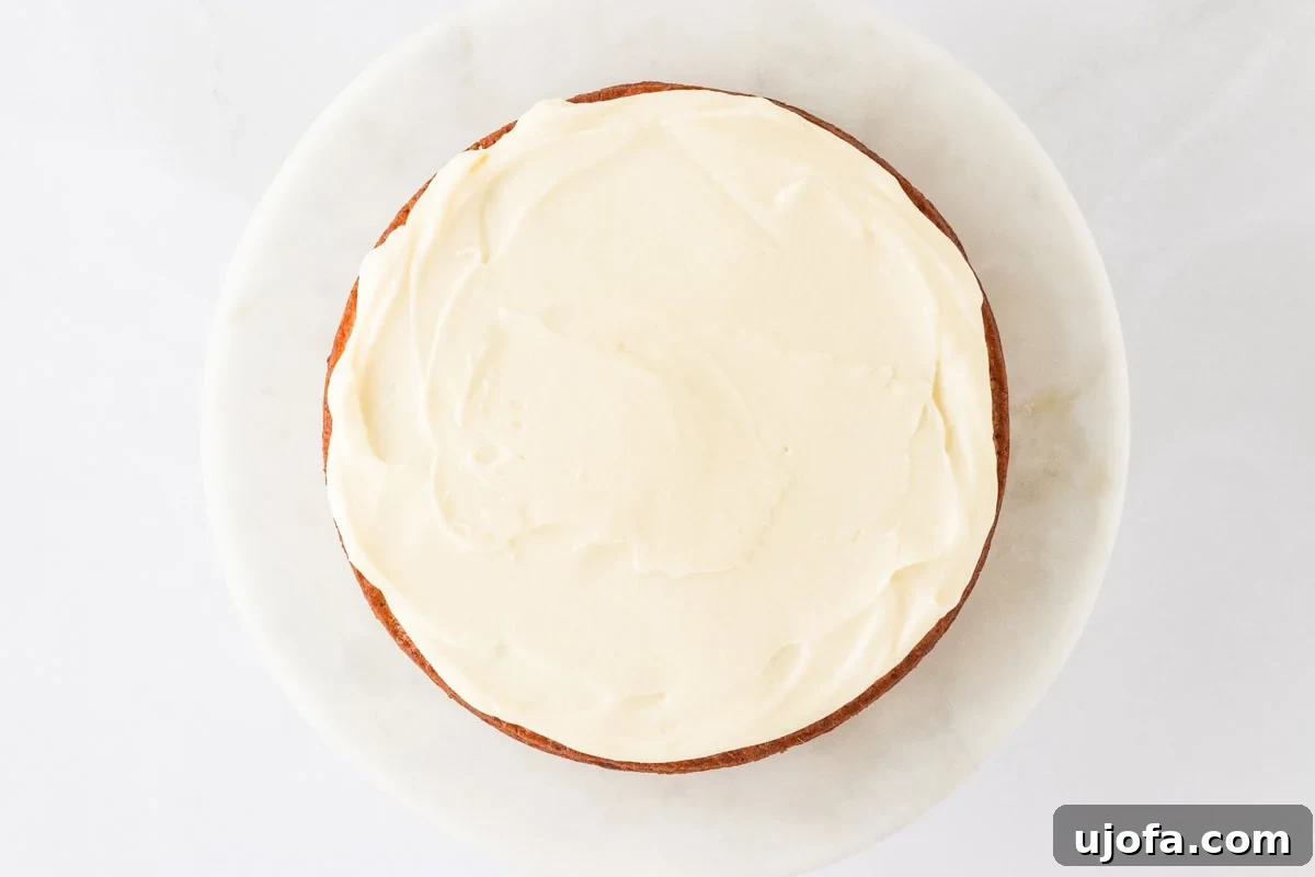 A single layer of gluten-free carrot cake fully frosted with smooth cream cheese frosting, ready for the next layer.