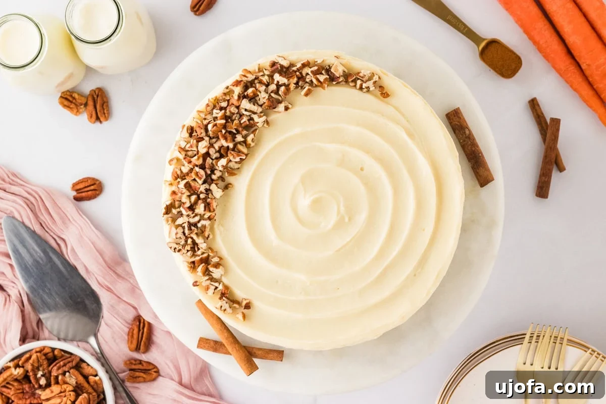 An overhead view of the fully frosted gluten-free carrot cake decorated with a swirl pattern and chopped pecans on one side, surrounded by cinnamon sticks, carrots, and pecans for styling.