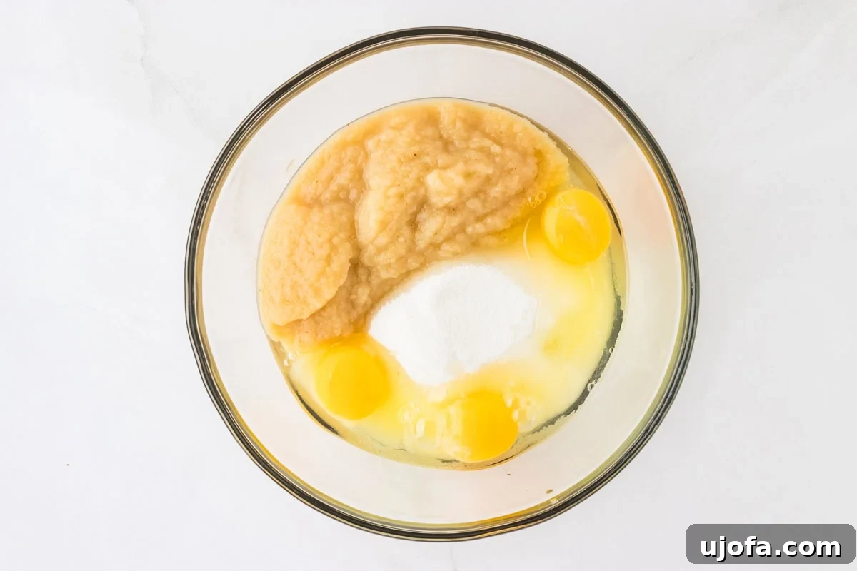 A mixing bowl containing eggs, sugar, applesauce, and oil as ingredients for the gluten-free carrot cake.