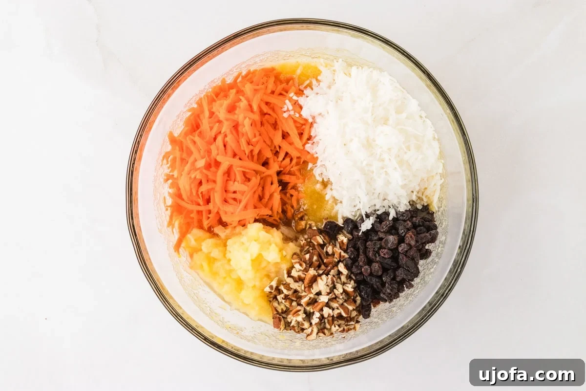 A mixing bowl filled with shredded carrots, crushed pineapple, shredded coconut, raisins, and chopped pecans, showcasing the cake’s flavorful add-ins.