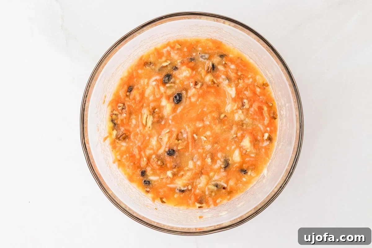 A mixing bowl with the carrot cake batter partially mixed, showing the vibrant orange color of the shredded carrots and other ingredients.