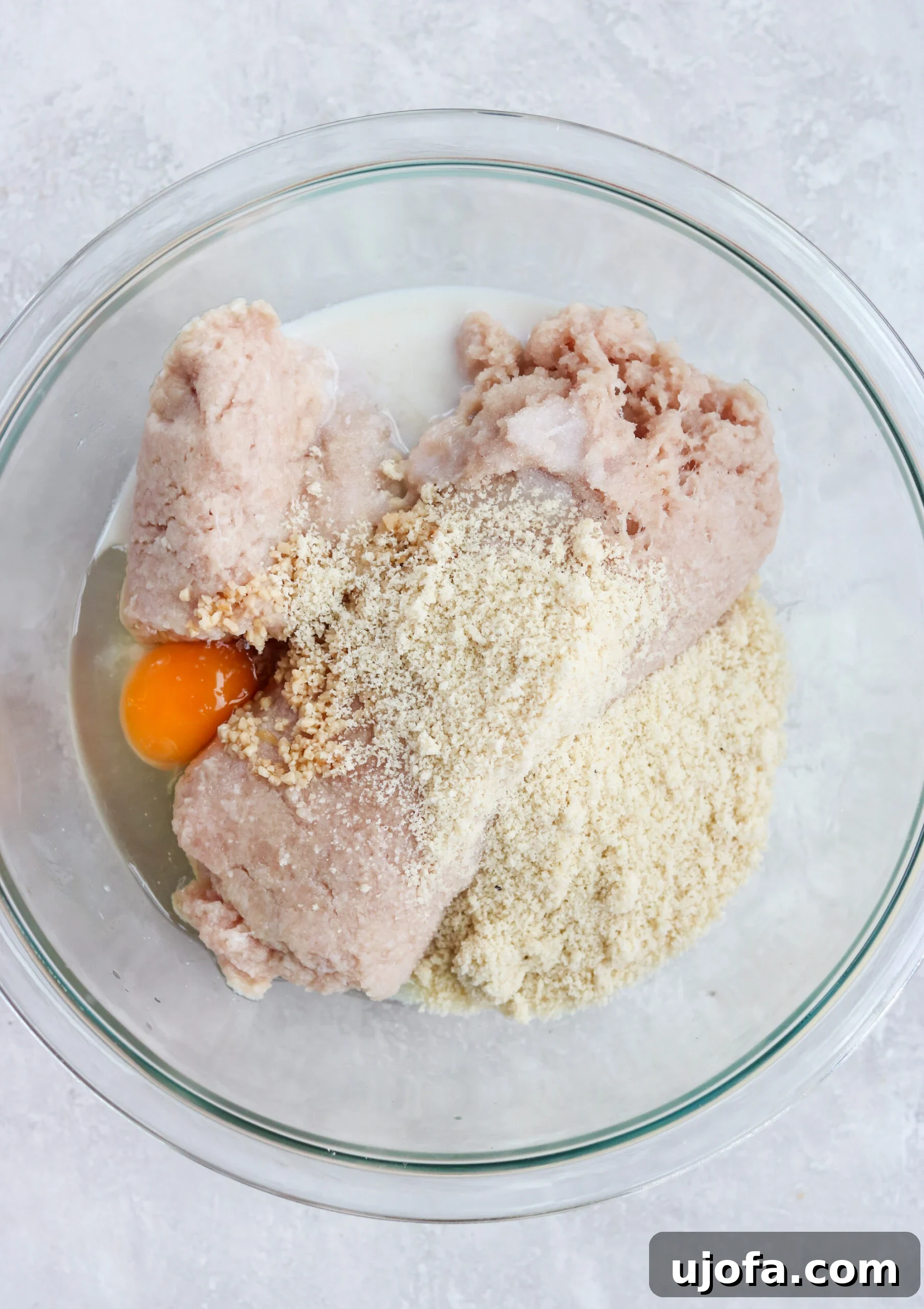 Paleo Butter Chicken Meatball Bake 2 prepping ground chicken with ingredients in a clear glass mixing bowl
