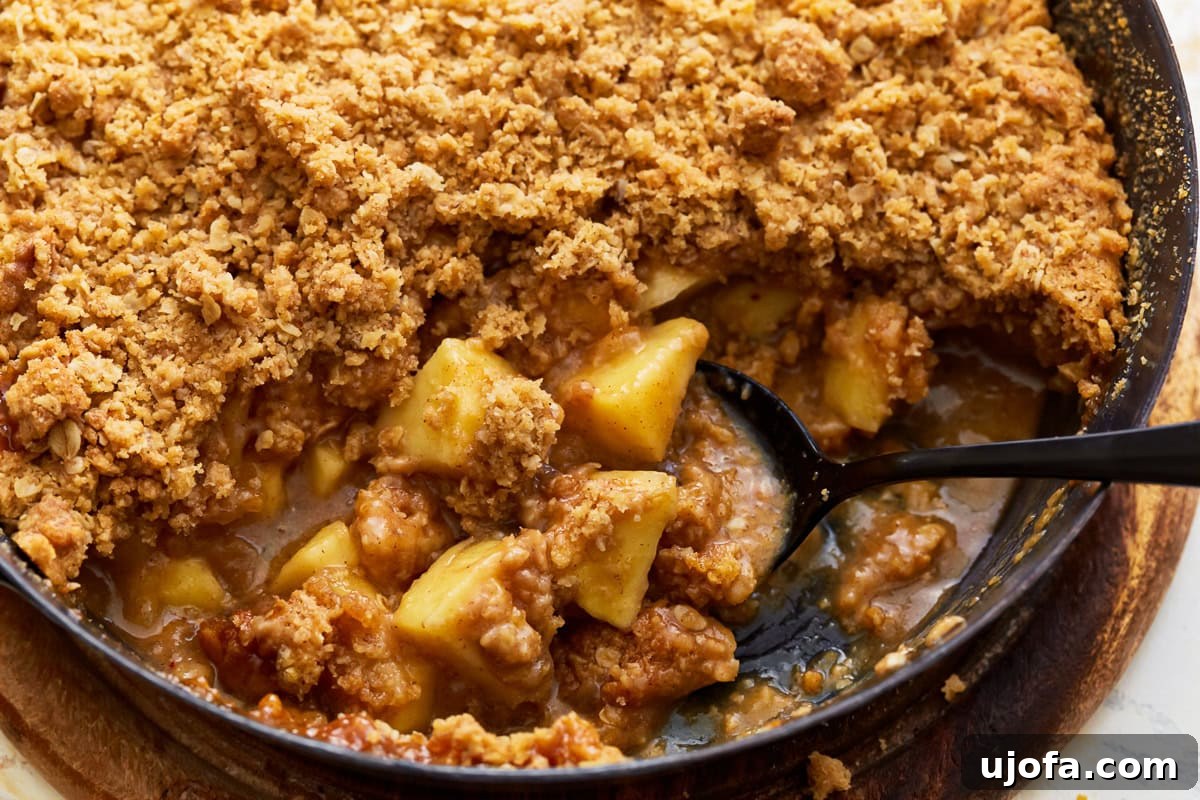 A serving spoon lifting a spoonful of warm gluten-free apple crisp from a glass baking dish, revealing the bubbly apple filling and crunchy topping.