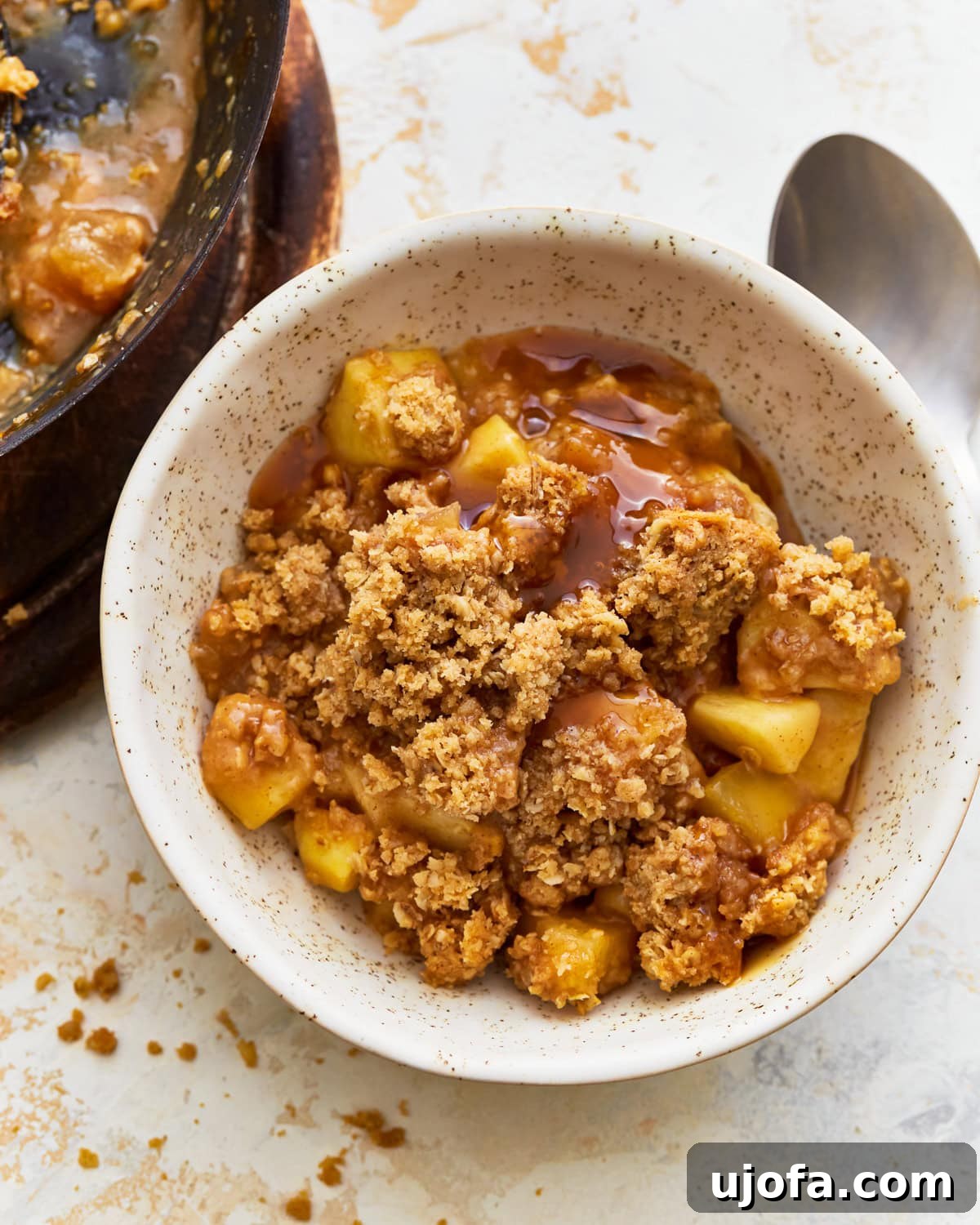 A cozy bowl of warm gluten-free apple crisp topped with a scoop of melting vanilla ice cream and a drizzle of caramel sauce.