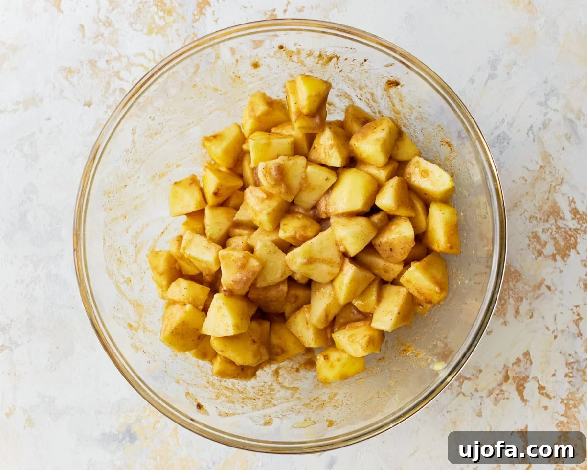 Freshly peeled and chopped apples in a large glass mixing bowl, ready for the filling ingredients.