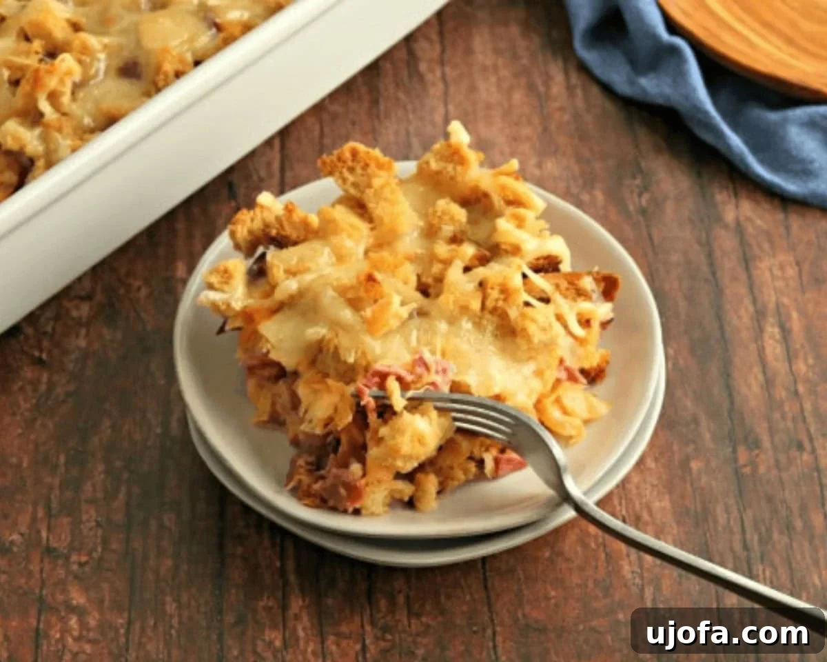 Ultimate Gluten-Free Reuben Bake 5 Slice of gluten-free Reuben casserole served on a small plate with a fork, showing layers of corned beef, sauerkraut, bread, and melted Swiss cheese.