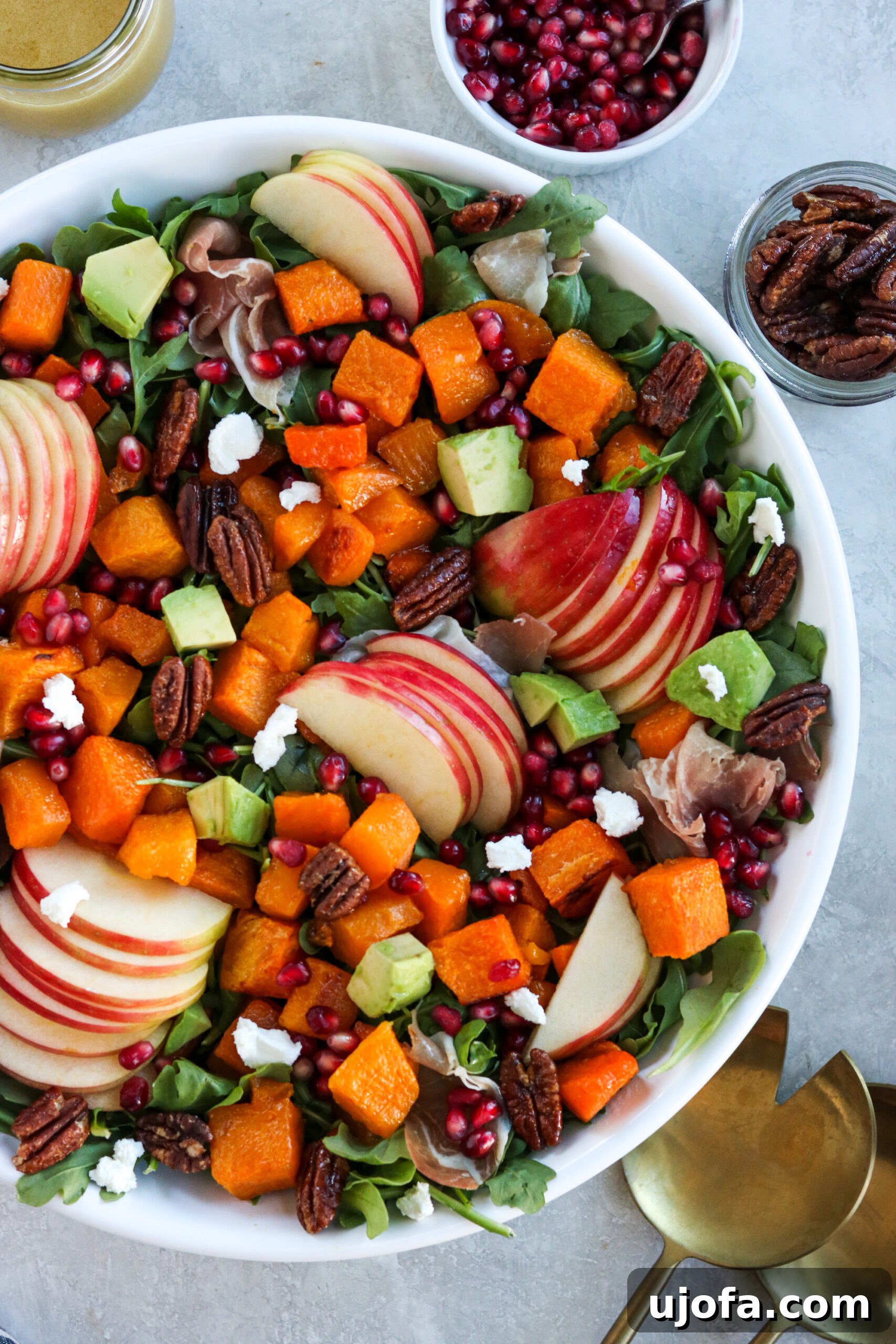 Autumn's Bounty Salad with Maple Apple Cider Vinaigrette 2 Autumn Harvest Salad in a white bowl surrounded by spoons, pomegranate seeds, pecans, and dressing – a perfect centerpiece for fall dining