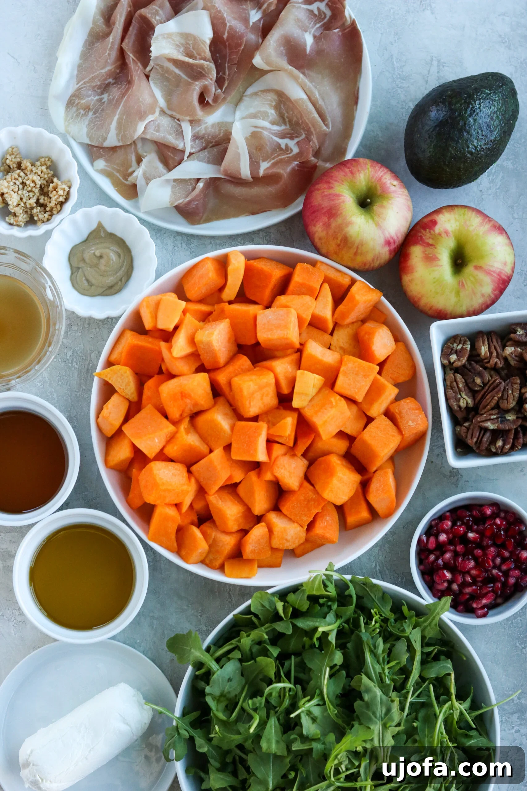 Autumn's Bounty Salad with Maple Apple Cider Vinaigrette 3 Ingredients for fall harvest salad including butternut squash, pomegranate seeds, candied pecans, prosciutto, apples, avocado, and arugula laid out beautifully