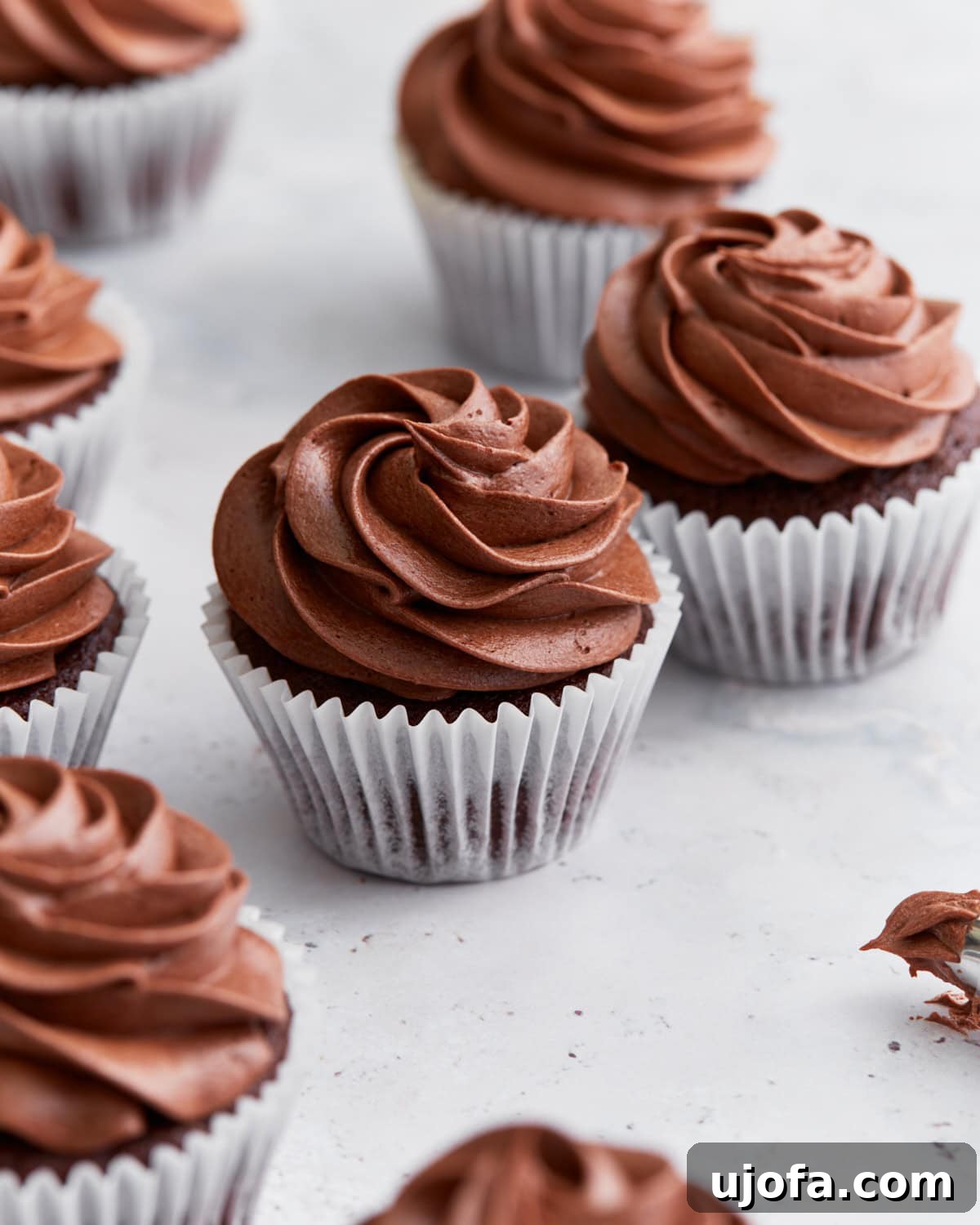 Guilt-Free Chocolate Indulgence 2 Close-up of several gluten-free chocolate cupcakes topped with swirled chocolate buttercream frosting in white cupcake liners on a white background.