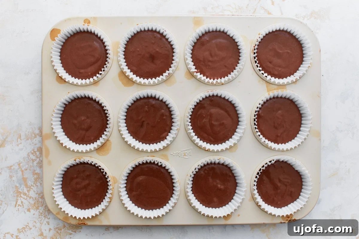 Guilt-Free Chocolate Indulgence 11 Muffin pan filled with white liners, each about two-thirds full of chocolate cupcake batter, ready to go into the oven.