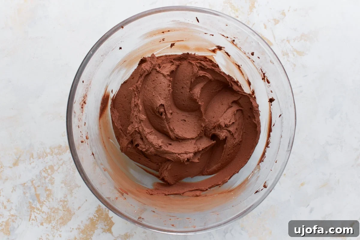 Guilt-Free Chocolate Indulgence 16 Thick, chocolate frosting forming as powdered sugar is added, shown in a mixing bowl with chocolate streaks.
