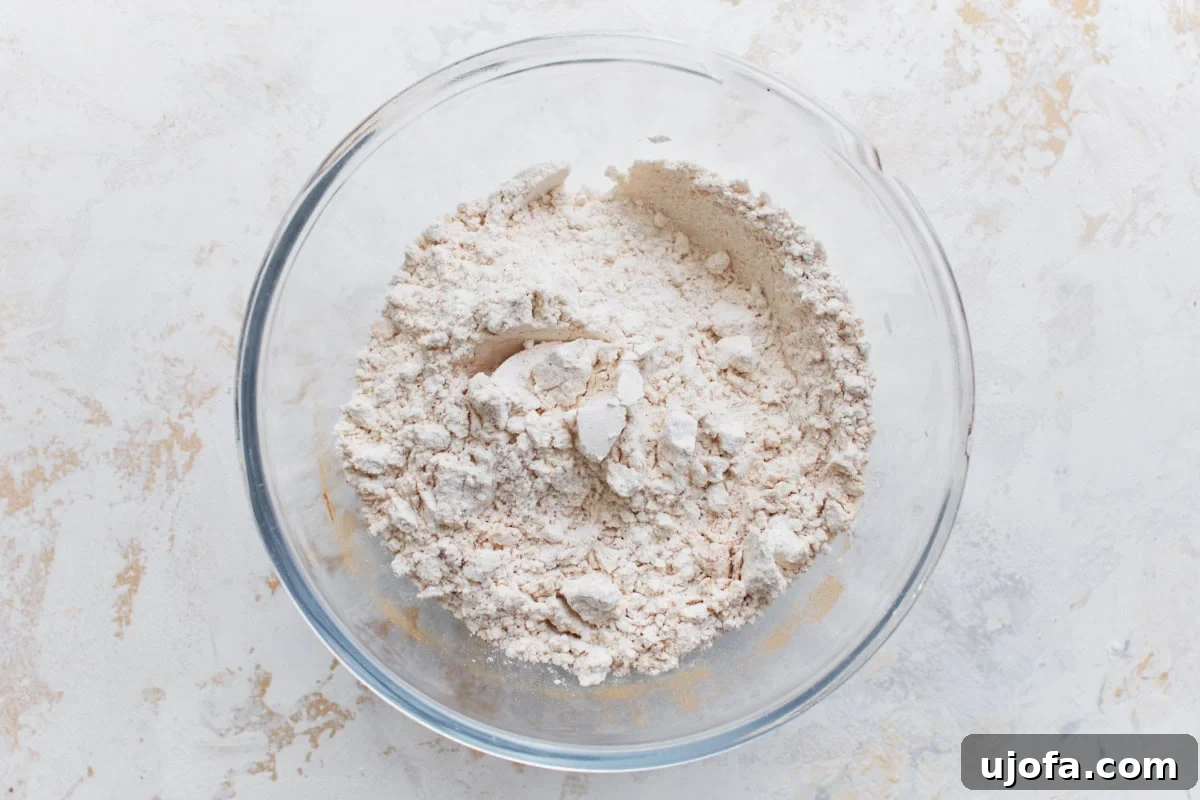 Guilt-Free Chocolate Indulgence 5 Overhead view of a clear glass bowl filled with mixed dry ingredients, including gluten-free flour and leavening agents, on a light textured surface.