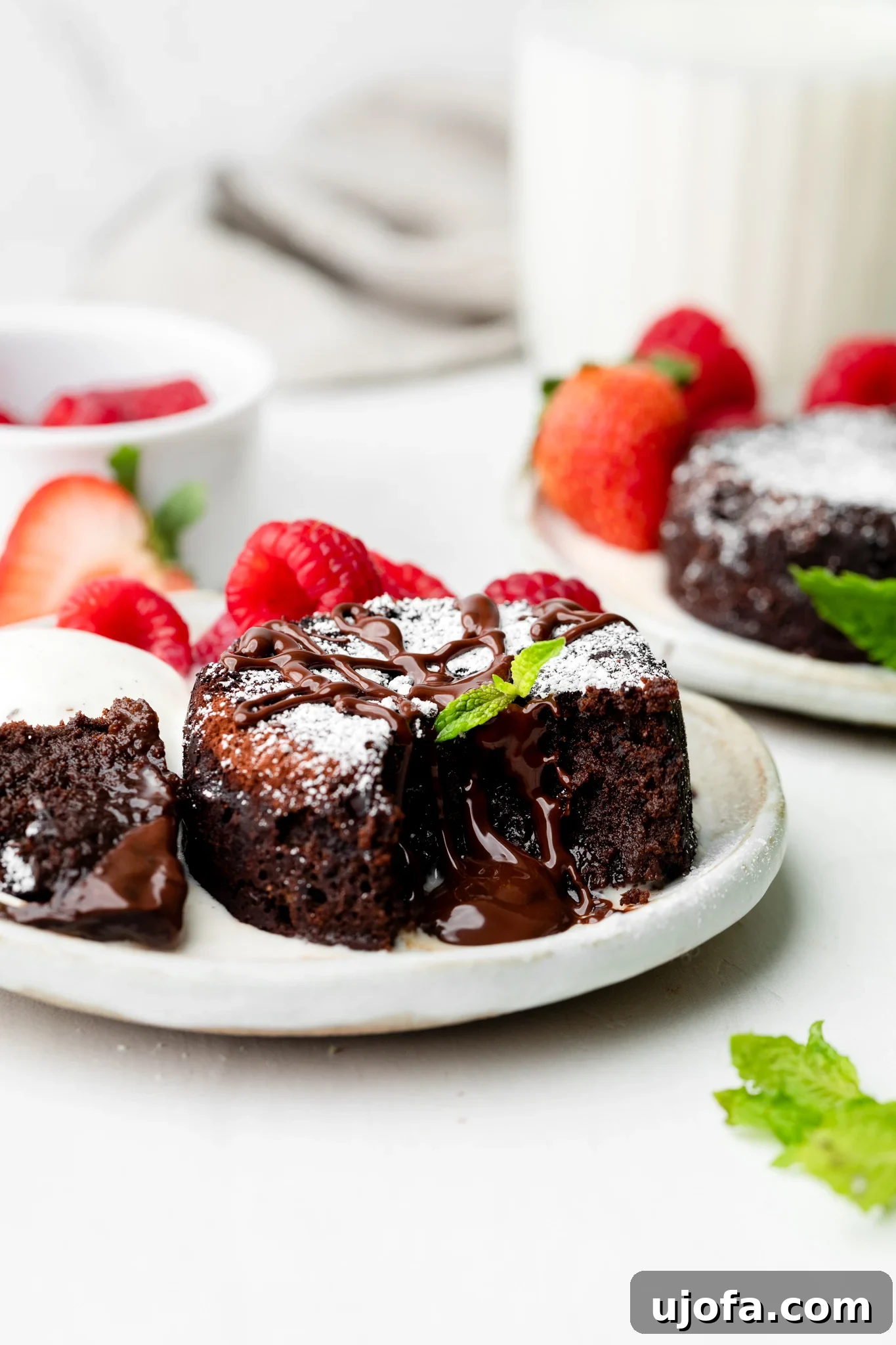 Gluten Free Molten Chocolate Lava Bites 2 Mini chocolate lava cake on a plate, garnished with fresh mint leaves and vibrant raspberries and strawberries in the background.