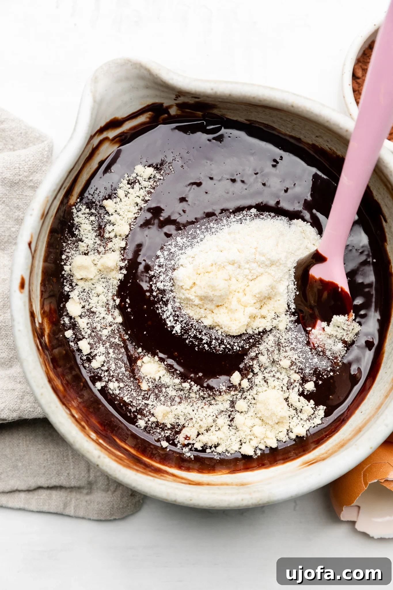 Gluten Free Molten Chocolate Lava Bites 5 Melted chocolate and almond flour in a mixing bowl, ready to be folded into the batter with a pink spatula.