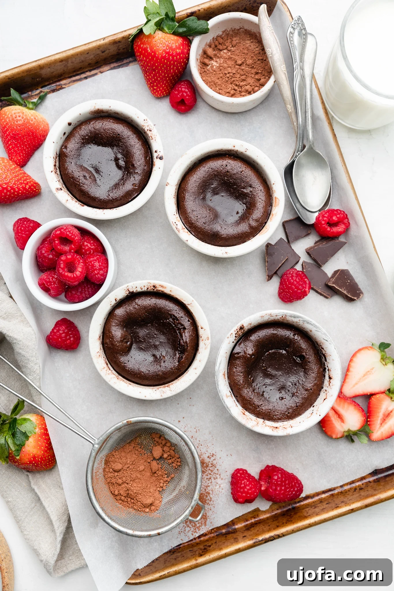 Gluten Free Molten Chocolate Lava Bites 6 Freshly baked gluten-free lava cakes cooling on a parchment-lined baking sheet, surrounded by berries.