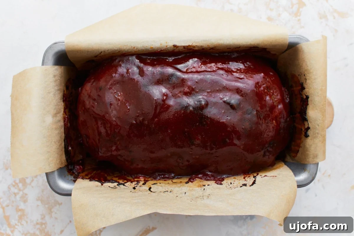 Freshly baked gluten-free meatloaf in a parchment-lined loaf pan, showing a glossy and caramelized glaze.