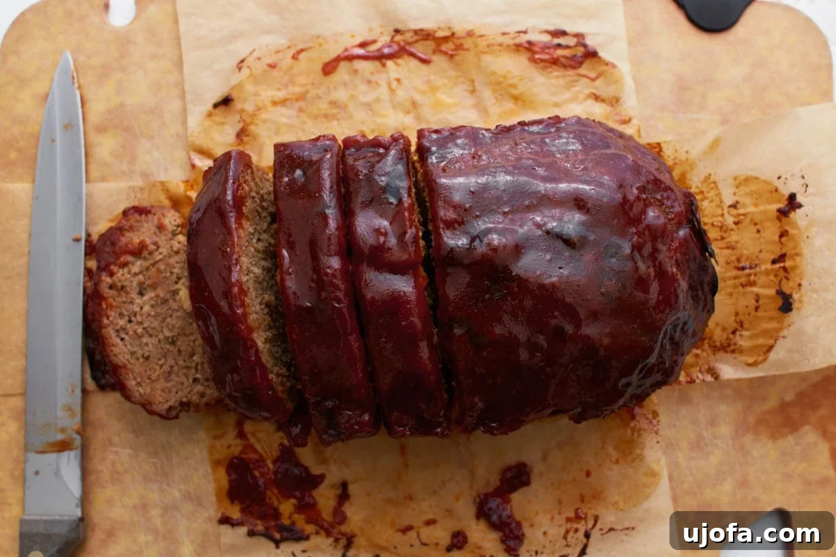 A sliced gluten-free meatloaf on a wooden cutting board, revealing the moist interior and glossy glaze on top.