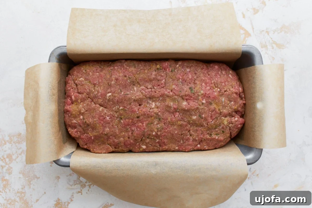 A loaf pan lined with parchment paper, filled with the raw gluten-free meatloaf mixture, shaped and ready for baking.