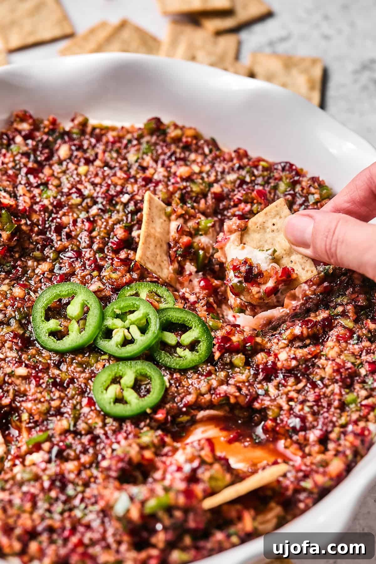 Effortless Dairy Free Cranberry Jalapeno Dip 11 a hand dipping a cracker into cranberry jalapeno dip