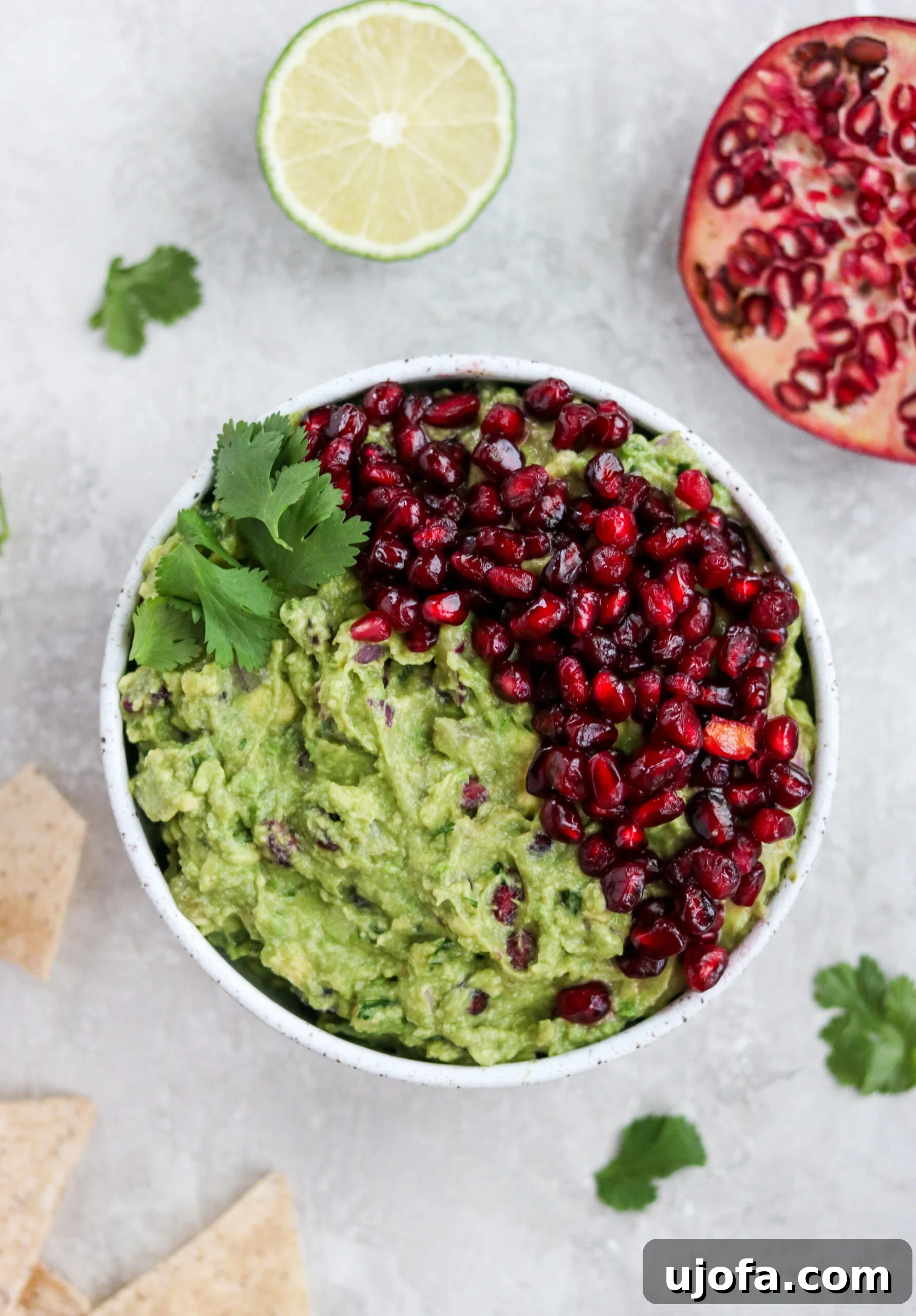 Vibrant Pomegranate Guacamole 4 Overhead view of a white bowl filled with healthy pomegranate guacamole, garnished with fresh cilantro