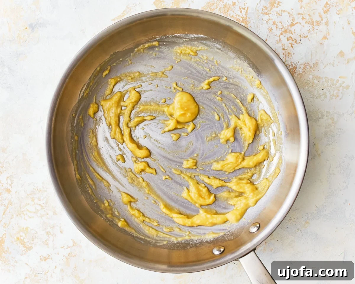 A smooth, golden gluten-free roux forming in a saucepan, being whisked.