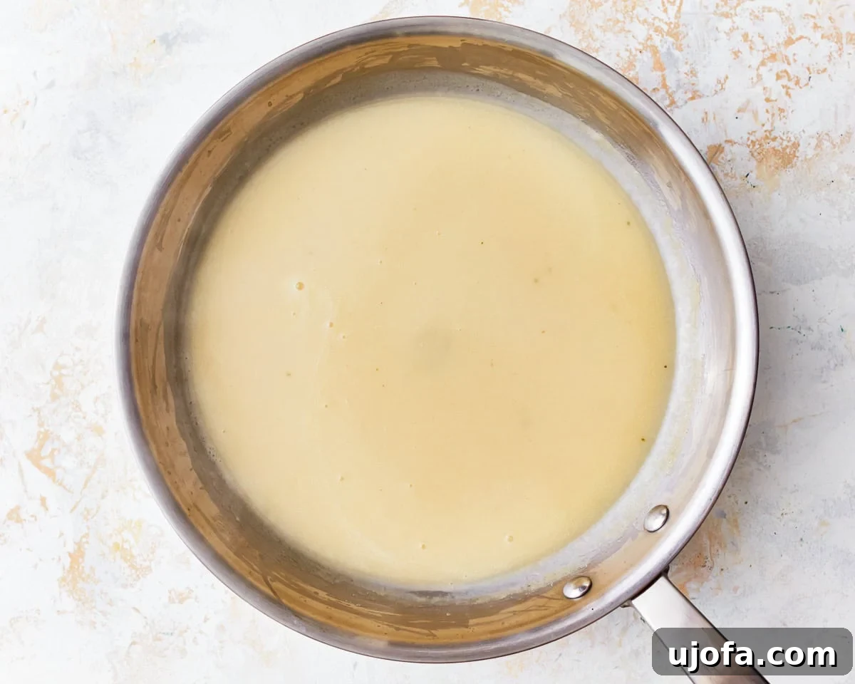 Gluten-free broth being added to the roux in a small saucepan, creating the gravy base.
