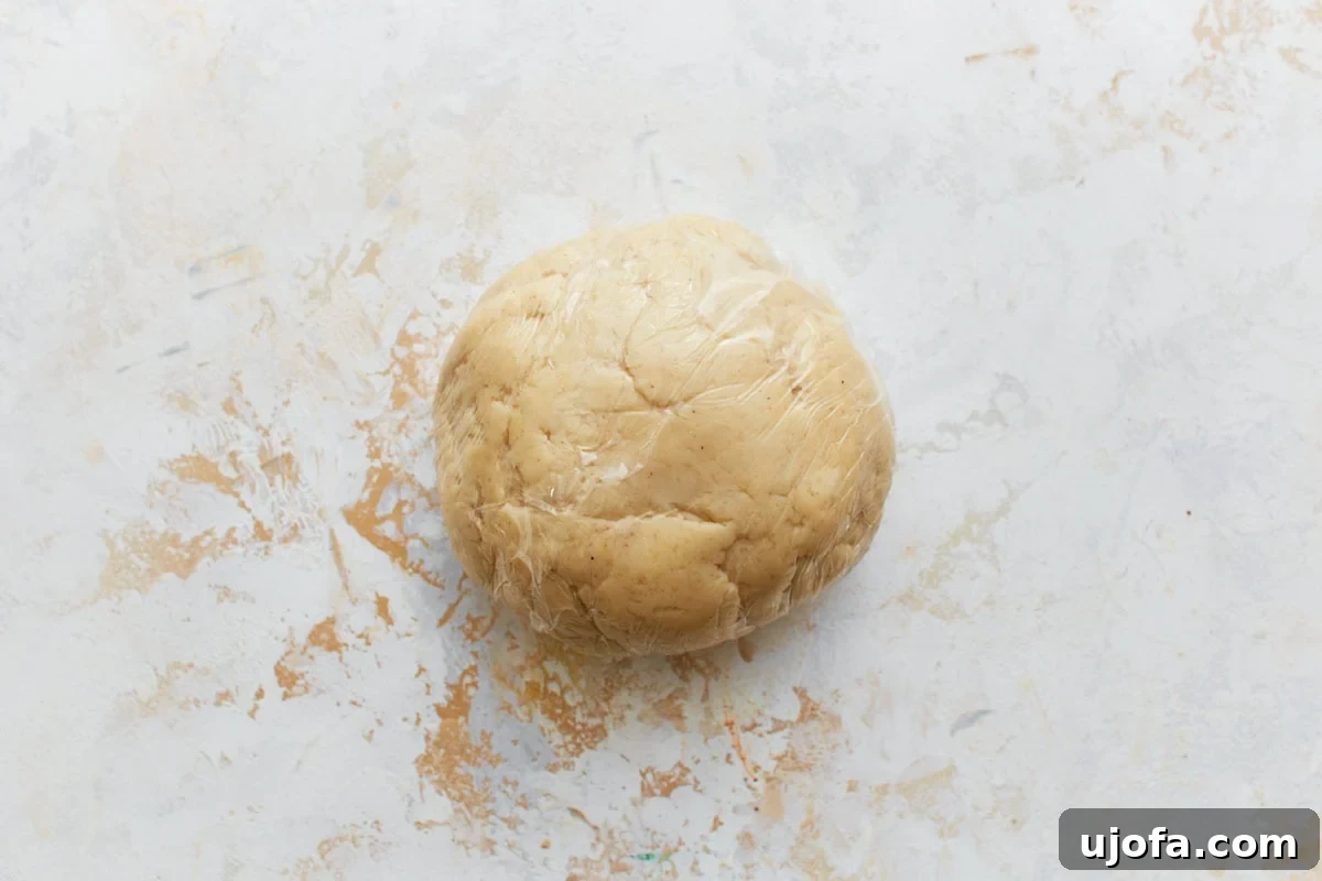 A smooth ball of gluten-free pie crust dough tightly wrapped in clear plastic wrap.