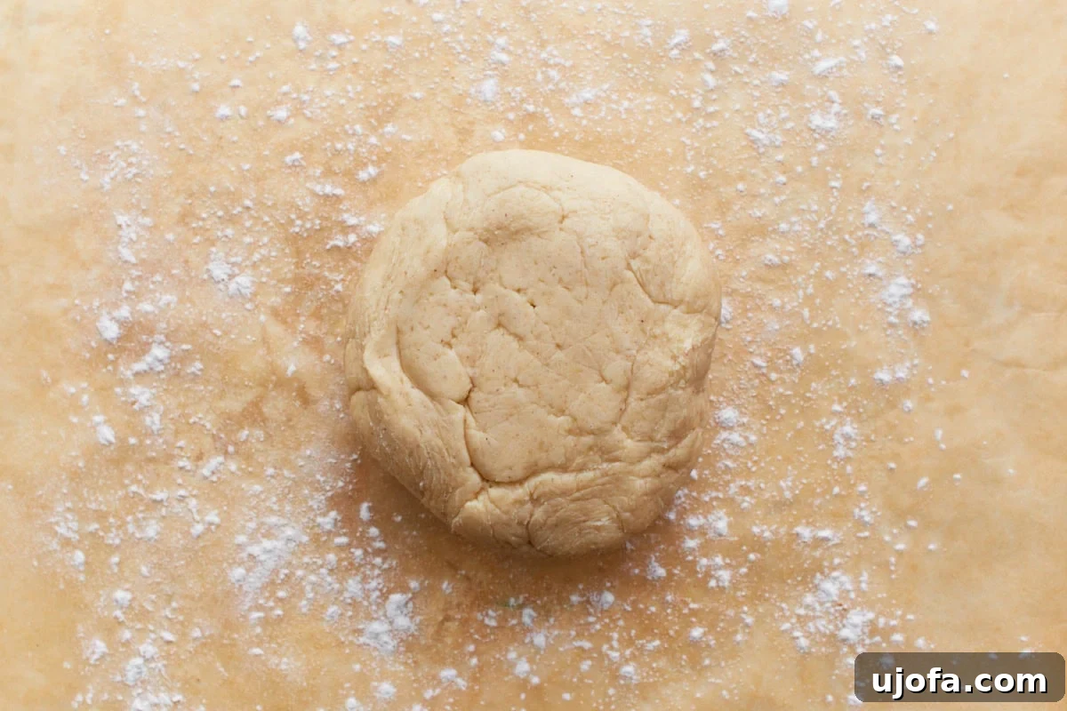 A chilled ball of gluten-free pie crust dough positioned on a sheet of parchment paper lightly dusted with gluten-free flour.