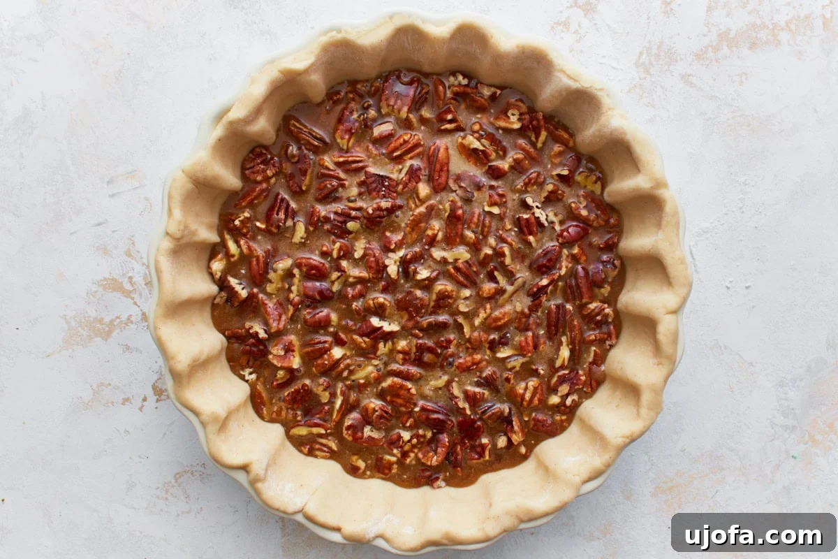 The rich, glossy gluten-free pecan pie filling being poured over the chopped pecans in the pie crust within a pie pan.