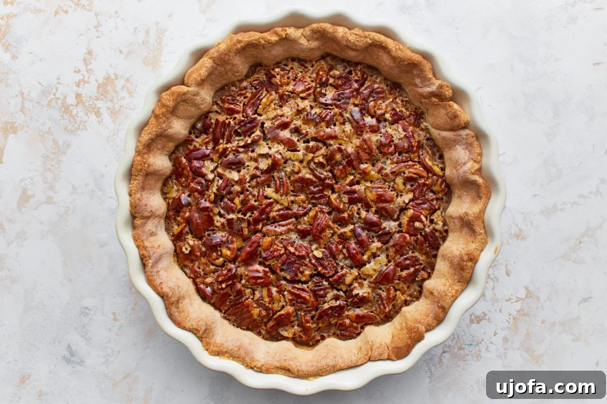 A gluten-free pecan pie freshly baked and cooling in its pie pan, showcasing a golden crust and set filling.