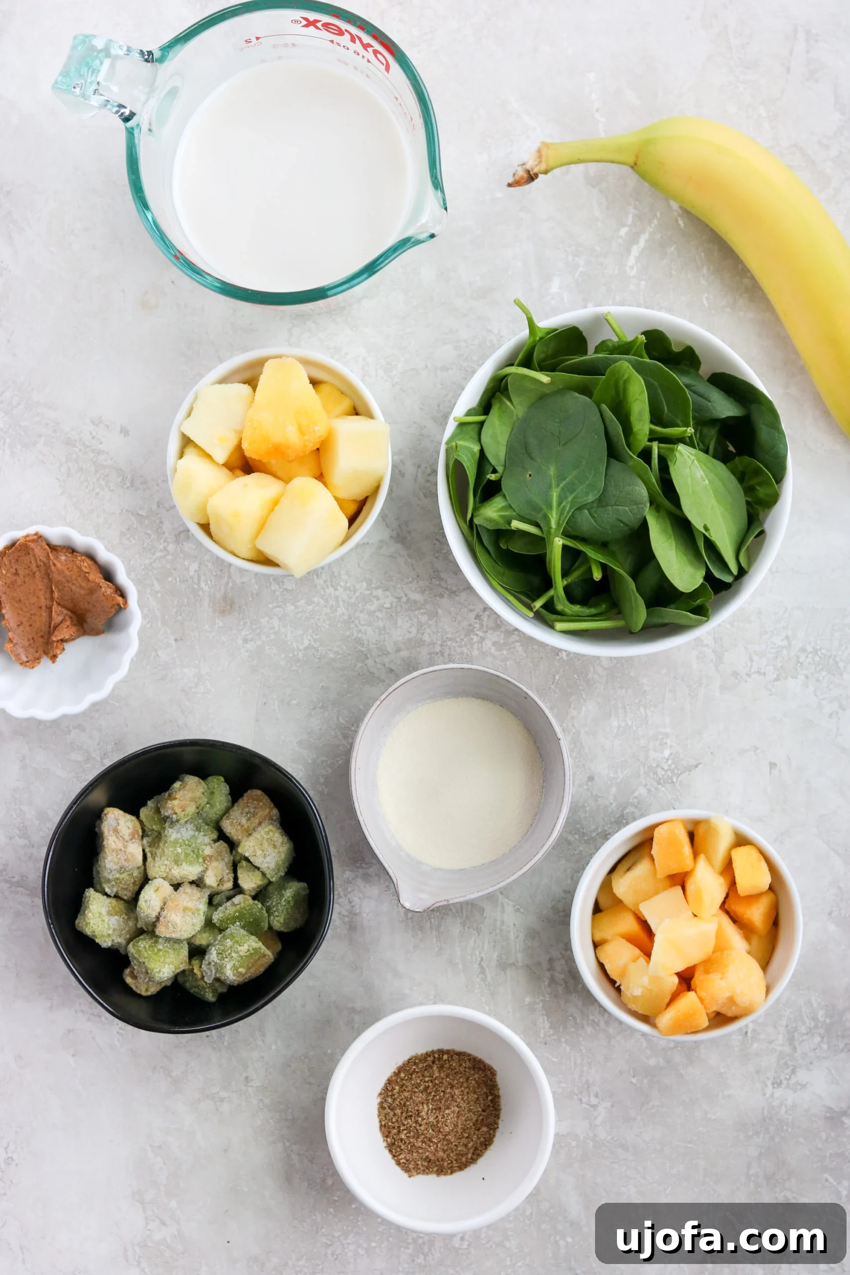 Paleo Green Goddess Elixir 3 Various fresh and frozen ingredients laid out for making a tropical green smoothie, including spinach, mango, pineapple, banana, and avocado