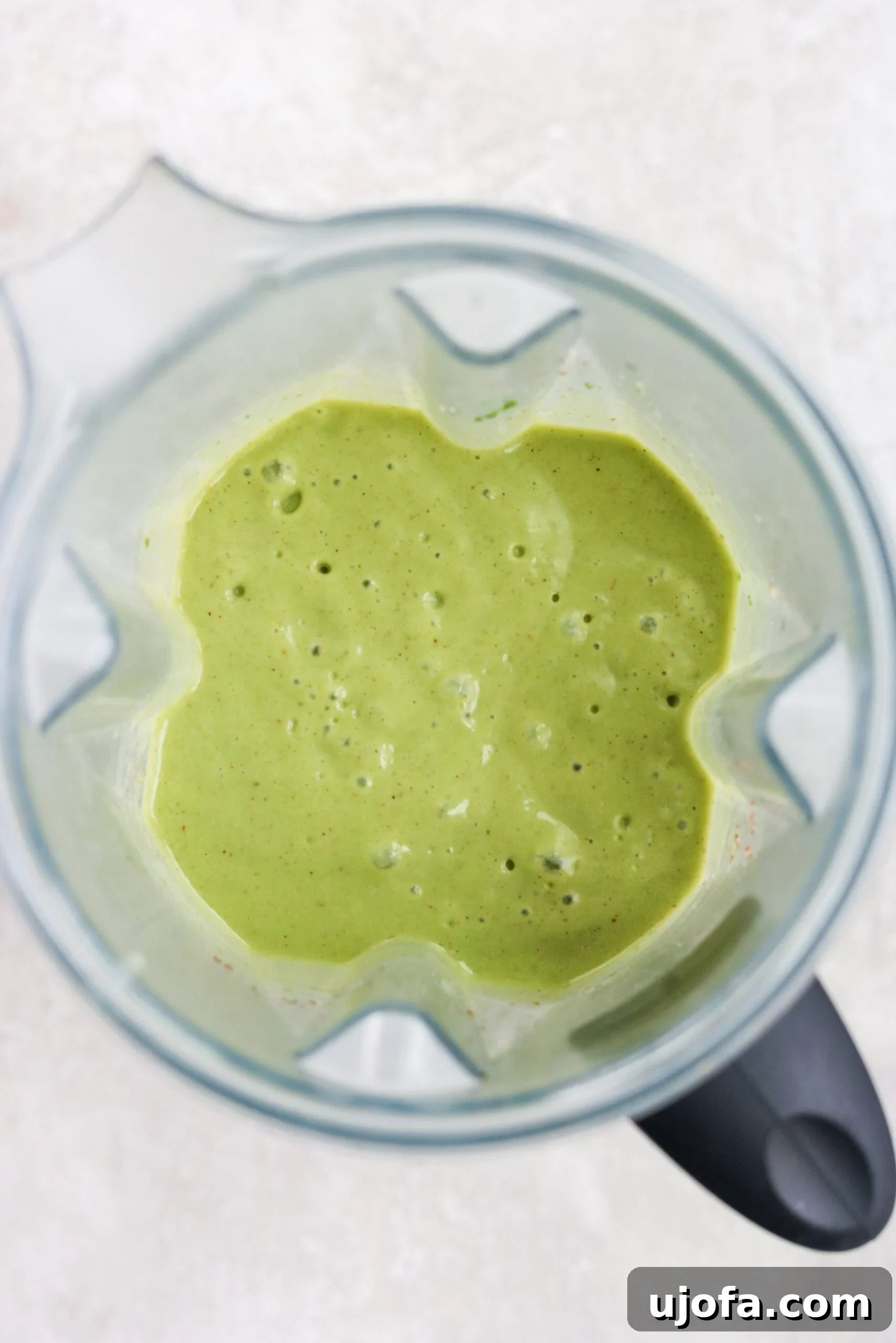 Paleo Green Goddess Elixir 5 A vibrant Green Goddess smoothie in a glass, freshly blended in a Vitamix blender, with a spoon for tasting