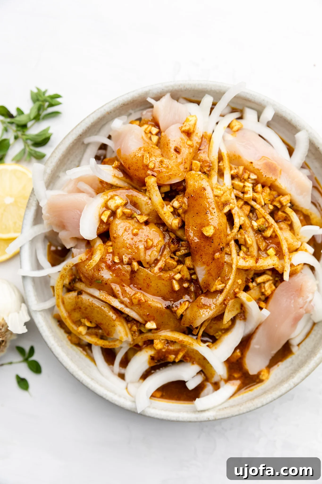 Sheet Pan Chicken Shawarma Power Bowls 4 Close-up of marinated chicken, onions, and minced garlic in a bowl, showcasing the rich color of the spices before cooking.