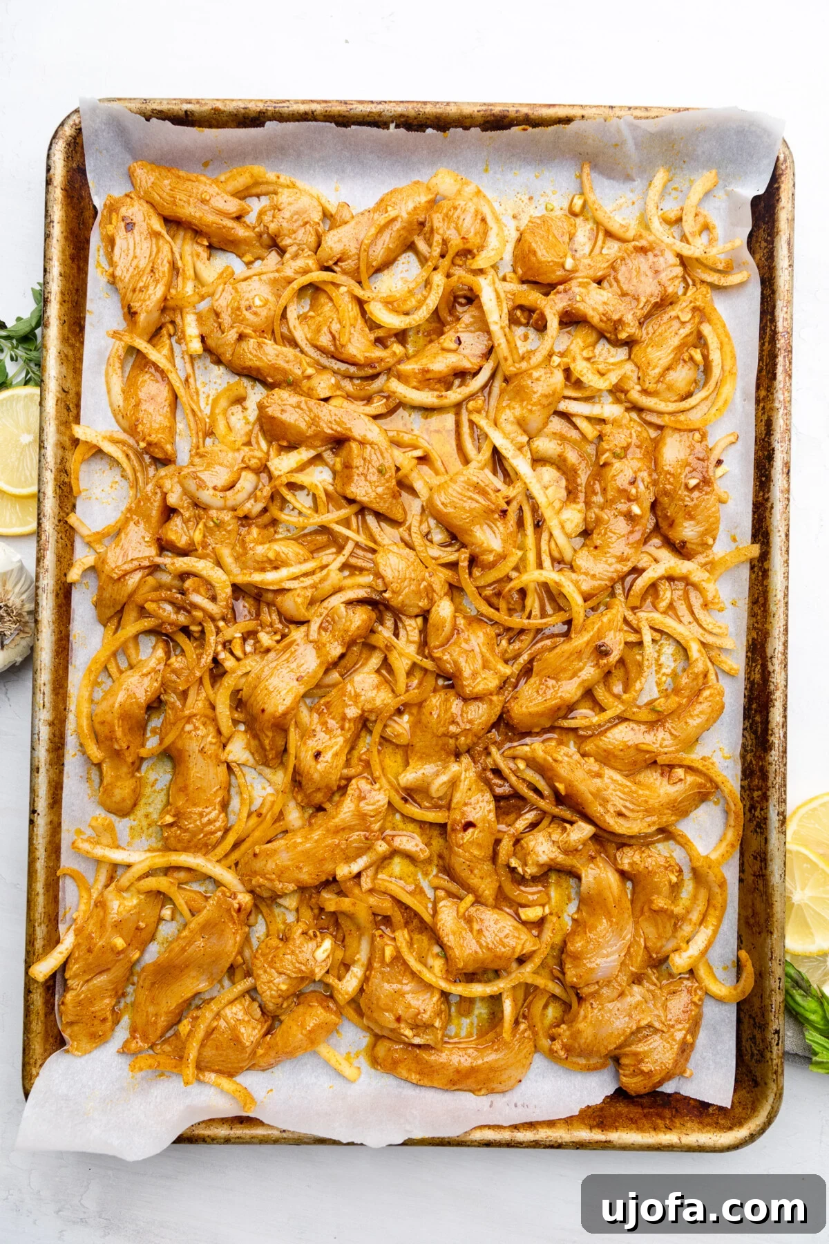Sheet Pan Chicken Shawarma Power Bowls 7 Thinly sliced marinated chicken and onions spread evenly on a parchment-lined baking sheet, ready for the oven.