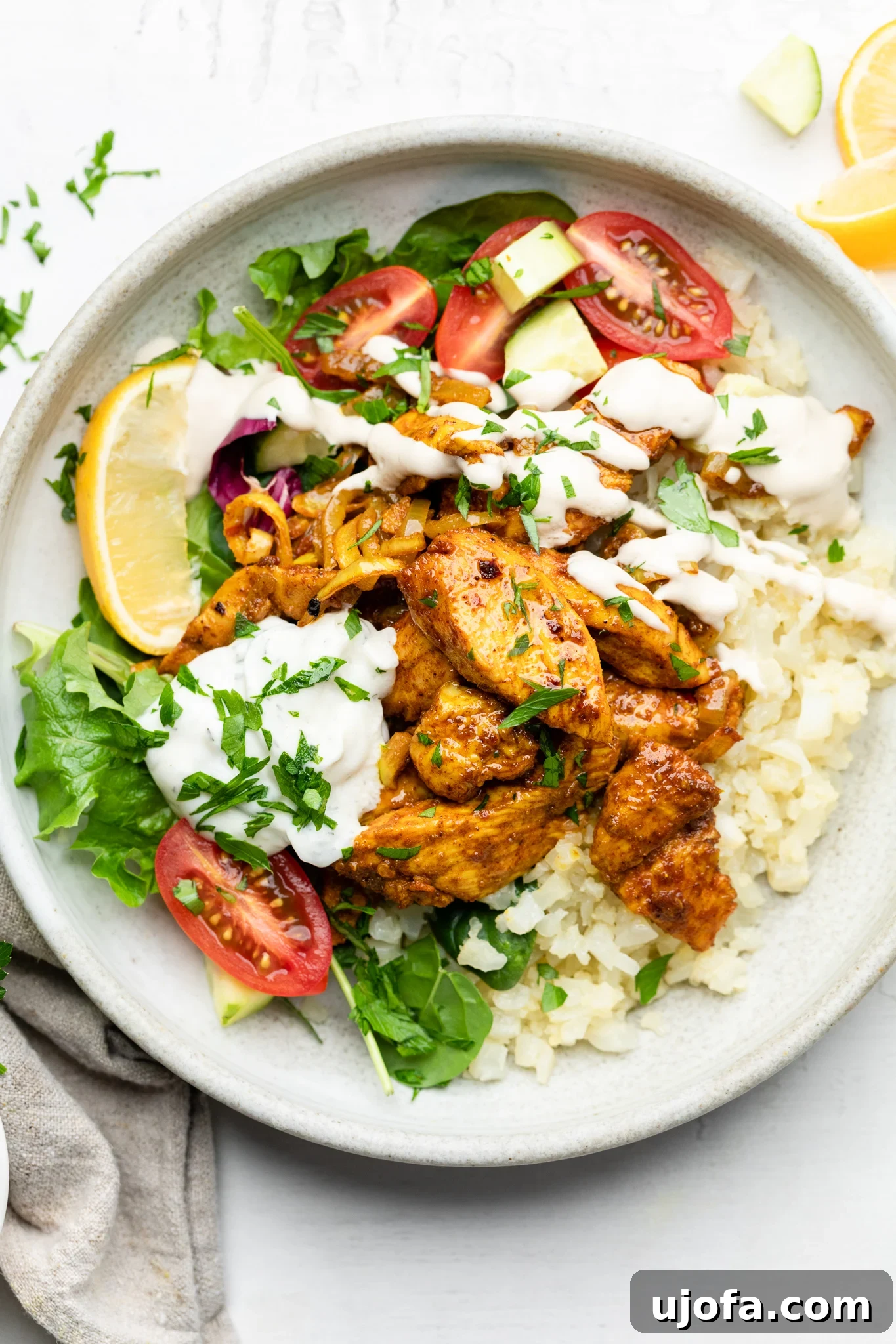 Sheet Pan Chicken Shawarma Power Bowls 9 A beautifully presented Sheet Pan Chicken Shawarma Bowl featuring cauliflower rice, diced tomatoes, fresh parsley, a lemon wedge, a dollop of tzatziki, and a generous drizzle of lemon tahini dressing.