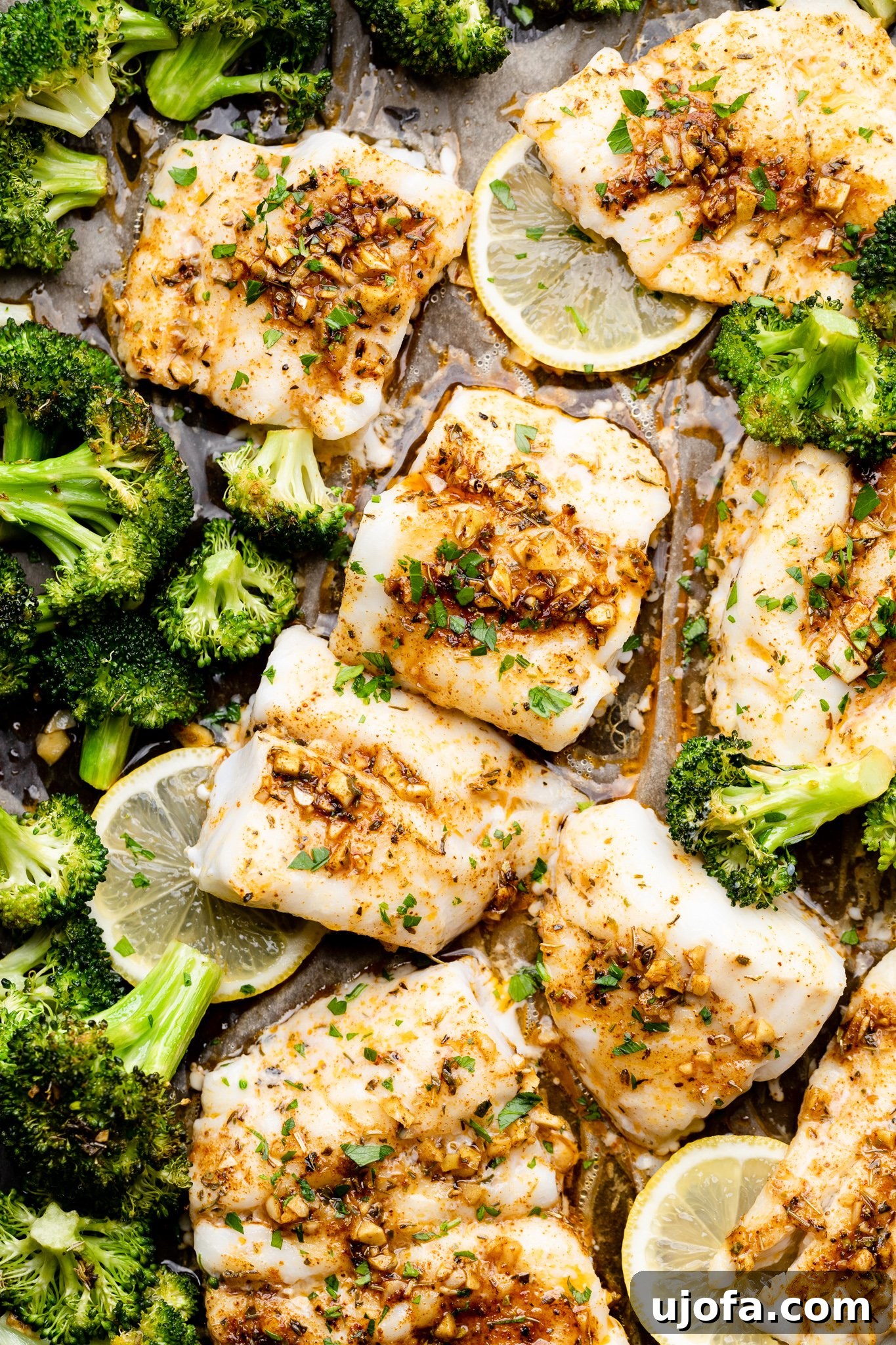 Cajun butter cod and broccoli on a sheet pan, garnished with fresh herbs and lemon wedges
