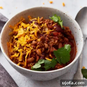 Closeup shot of a white bowl filled with gluten-free chili, topped with parsley and shredded orange cheese.