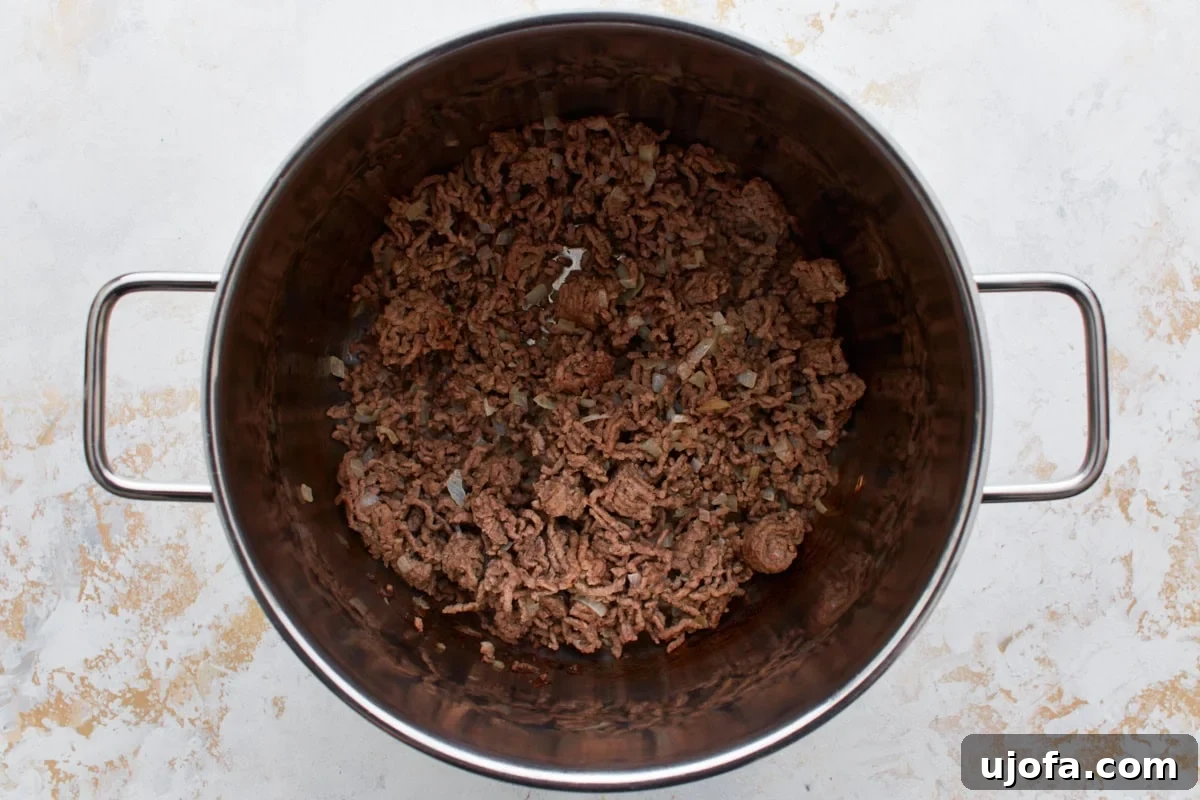 Ground beef crumbled and browning in a large stainless steel pot with died onions