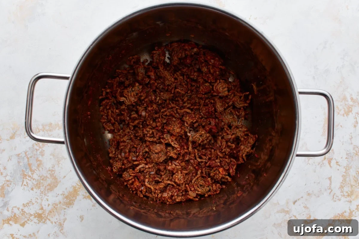 Crumbled and browned ground beef in a large stainless steel pot with died onions and a spice mixture.