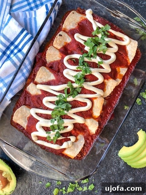 Delicious Paleo Beef Enchiladas freshly baked in a rectangular baking dish, topped with fresh avocado slices and chopped cilantro. The dish rests on a wooden surface.