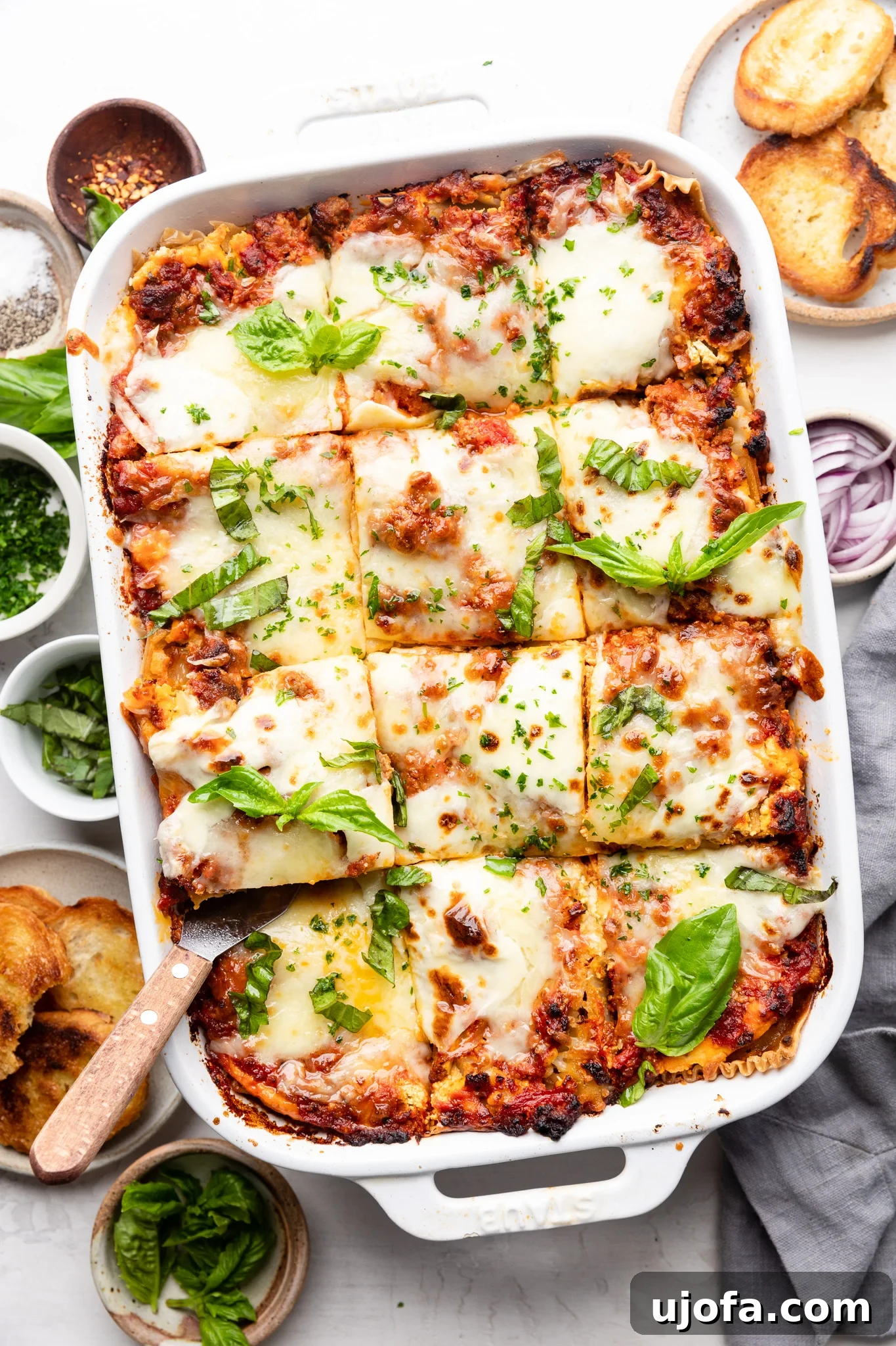 Gluten-free lasagna in a white casserole dish with fresh basil on top and slices of toasted bread on the side