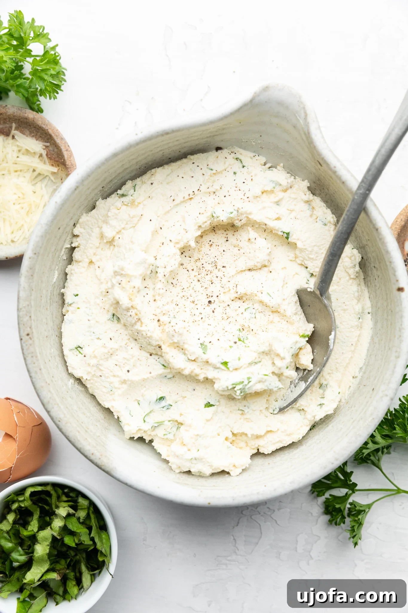 A creamy mixture of ricotta cheese, egg, and fresh herbs in a gray bowl, ready for layering in gluten-free lasagna