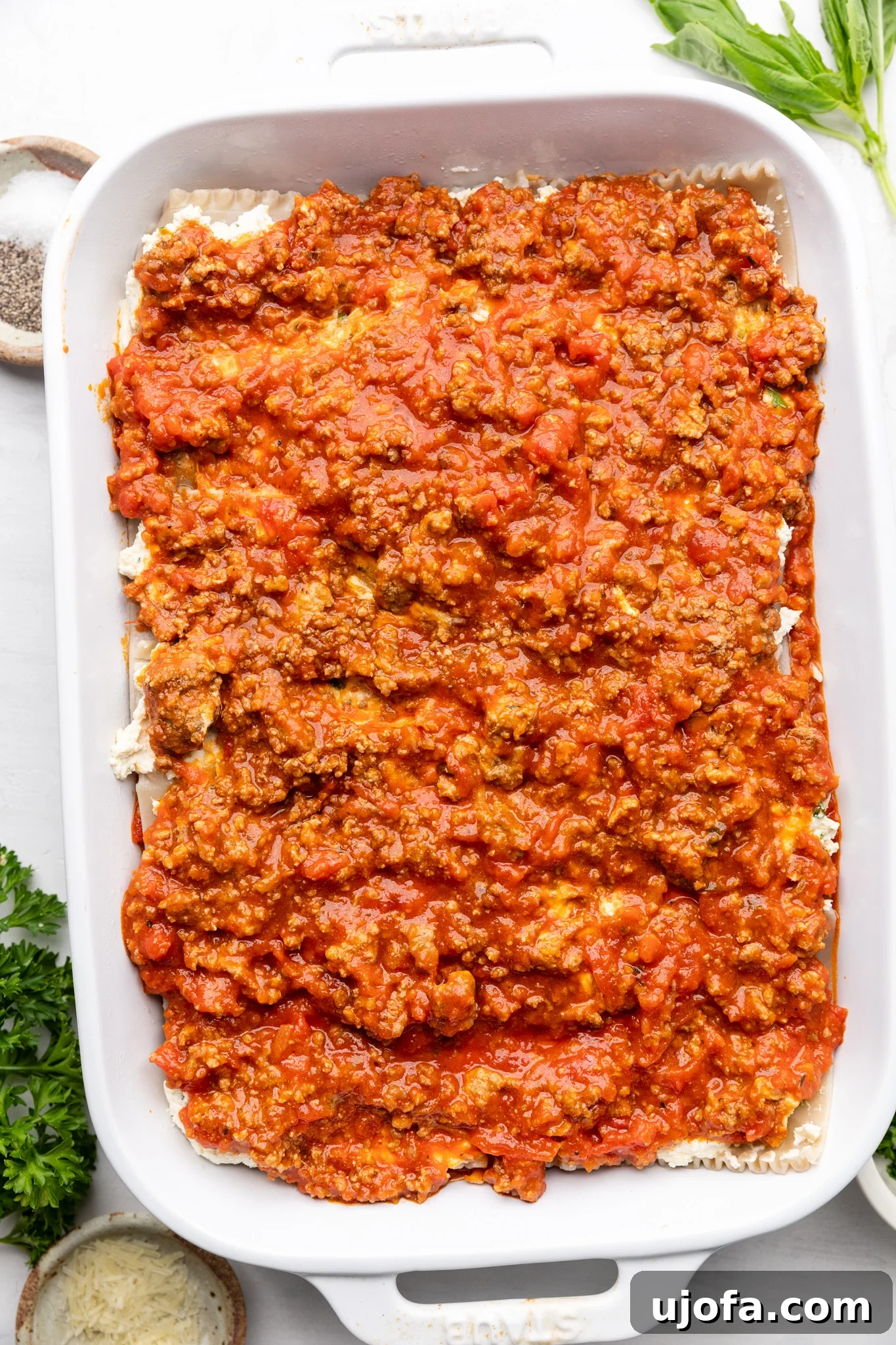 Beautifully layered gluten-free lasagna in a white casserole dish, showing the distinct layers of noodles, sauce, and cheese before baking
