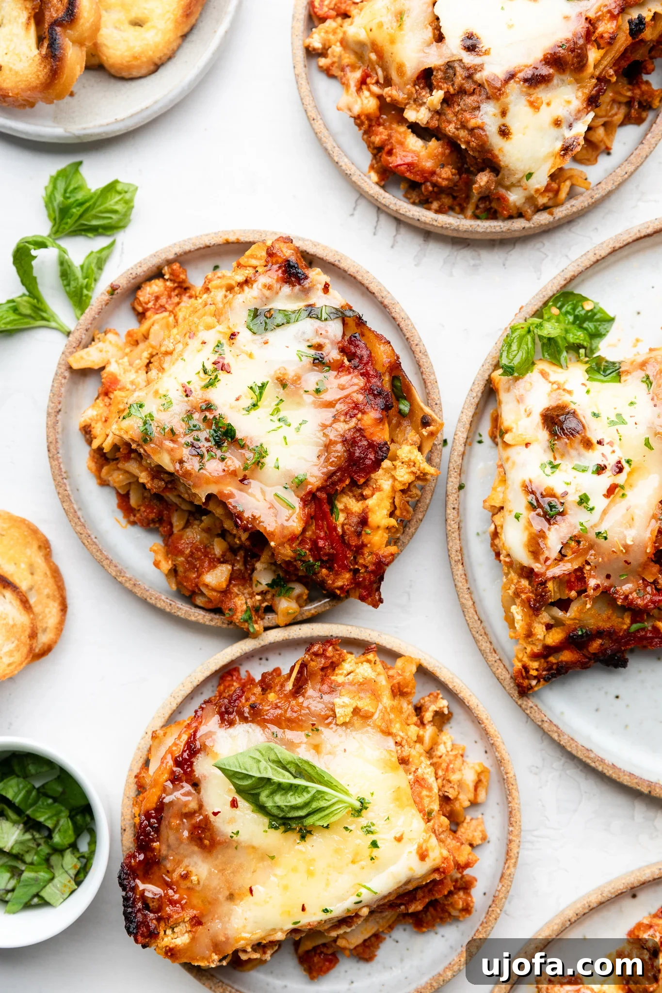 Four plates, each with a slice of gluten-free lasagna garnished with fresh basil, ready to be served