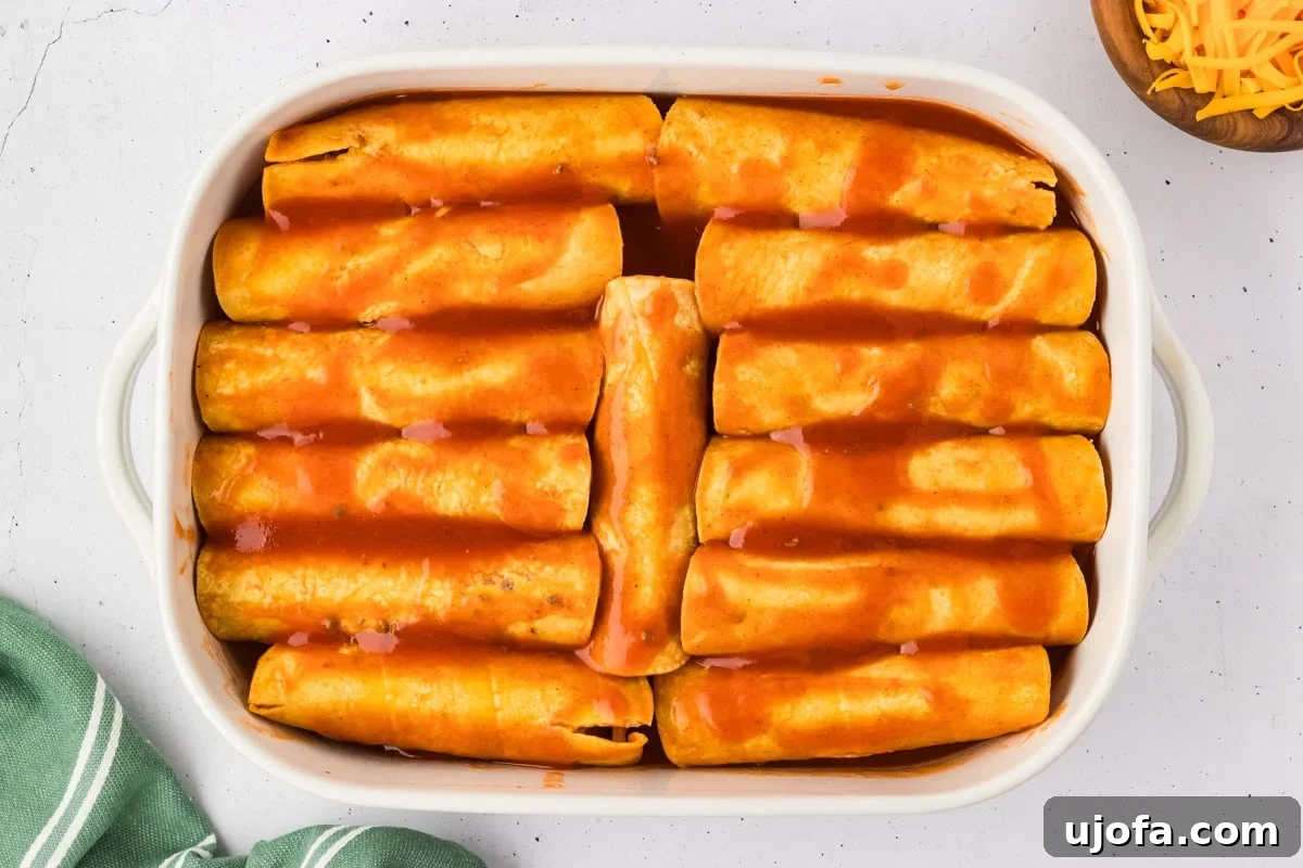 A 9x13 baking dish, brimming with neatly rolled enchiladas, is fully covered with an additional layer of rich red enchilada sauce, perfectly prepped and ready for its oven journey.