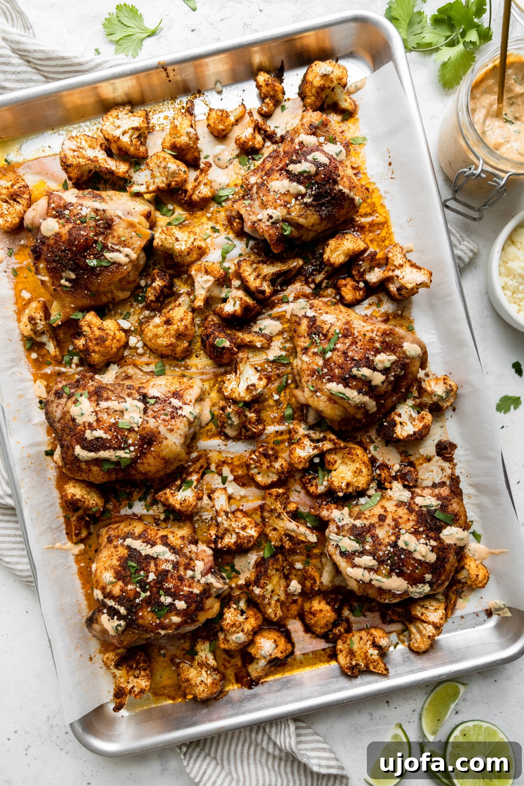 A glistening silver sheet pan piled high with golden-brown roasted cauliflower and perfectly charred chicken thighs, ready to be transformed into delicious street taco bowls.